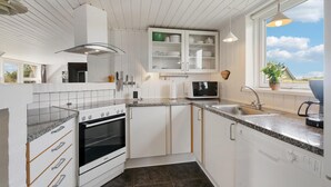 Moderni keittiö, jossa on valkoiset kaapit, sisäänrakennettu uuni, mikroaaltouuni ja pesuallas. Ikkunasta on näkymä ulos.