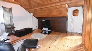 Una habitación acogedora en el ático con vigas de madera, televisión, sofá y una pequeña mesa.