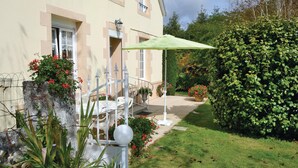 Ein Gebäude mit einer überdachten Außenbereich-Sitzgelegenheit, einem weißen Zaun und einem gepflegten Garten mit verschiedenen Pflanzen und Blumen.