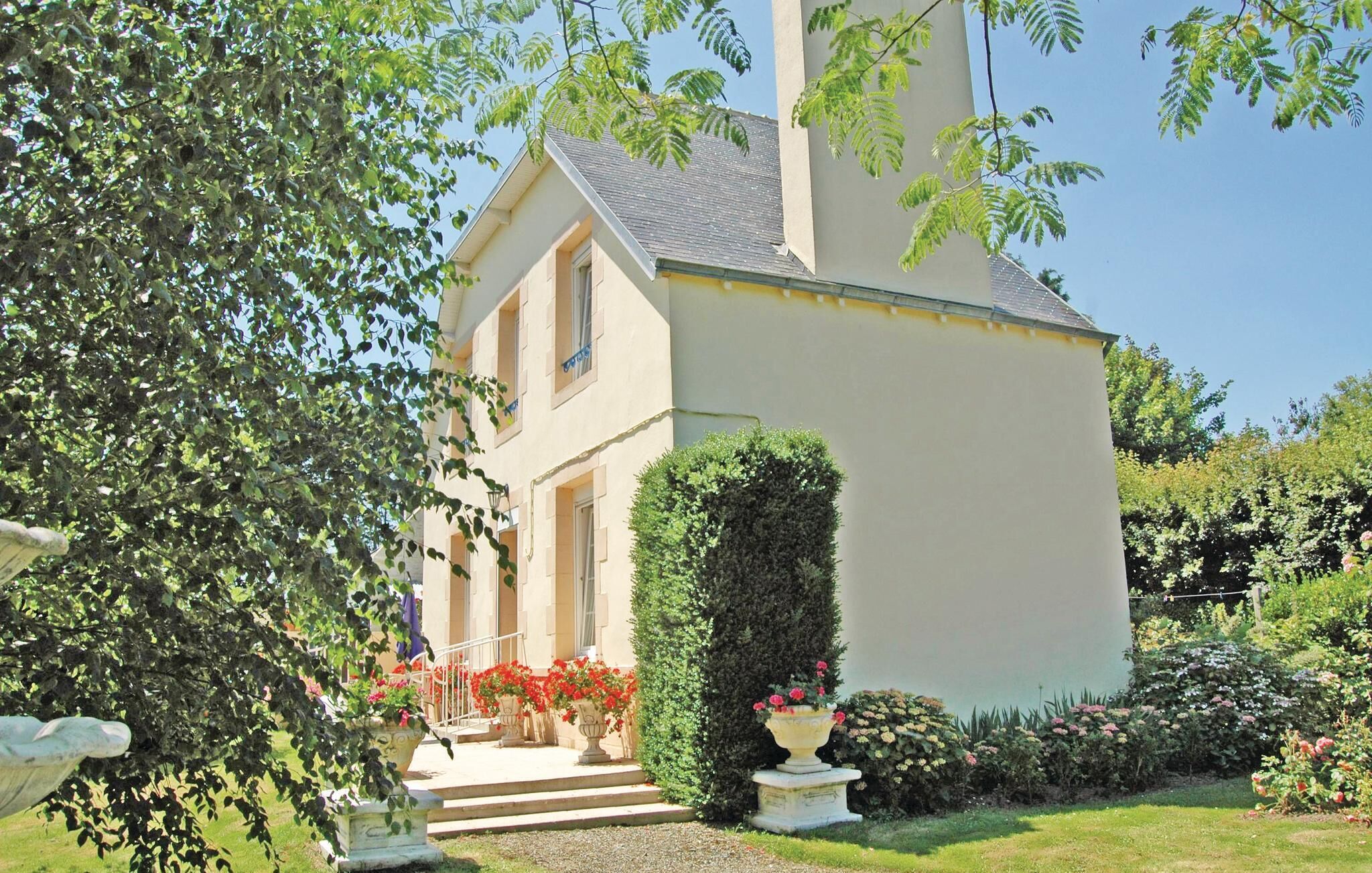 Une maison à deux étages avec un jardin bien entretenu, un chemin de pierres menant à l’entrée et une variété de plantes à fleurs.