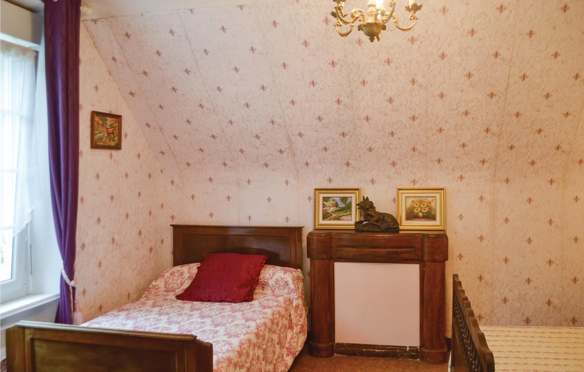 A bedroom with a bed, a nightstand, a chandelier, and patterned wallpaper.