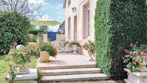 Ein Gebäude mit feierlichem Eingang, Stufen, die zu einer Tür führen, und einem gepflegten Garten mit Pflanzkübeln und Blumen.