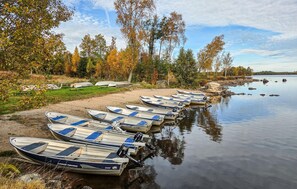 Een rij kleine bootjes langs een zandstrand, aan een rustig waterlichaam, met bomen op de achtergrond.