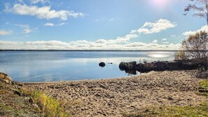 Una spiaggia con un lago tranquillo, cieli sereni e alberi in lontananza.