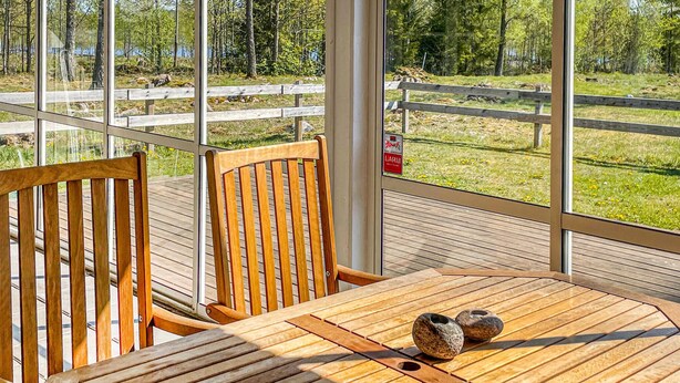 Un terrazzo in legno con tavolo e sedie, affacciato su un'area recintata con alberi e un corso d'acqua.