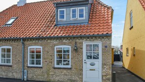A brick building with a red-tiled roof, a white door with a brass plate, and a small window with a decorative pattern. - 3 bedroom stunning home in Sæby (Sæby)