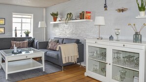 A living room with a grey sofa, a white coffee table, and a cabinet with glass doors containing glassware. - 3 bedroom stunning home in Sæby (Sæby)