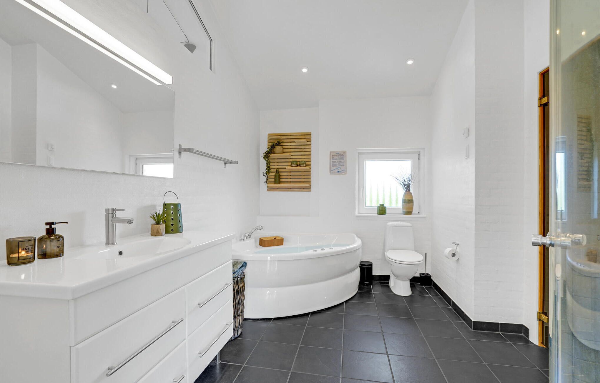 Un baño moderno con un espejo grande, una bañera independiente, un inodoro y un mueble de tocador con cajones.