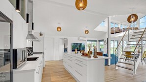 A modern kitchen with white cabinetry, a central island, and a dining area with a staircase leading to an upper level. - Beautiful home in Skjern with sauna (Skjern)