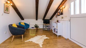 A cozy living room with a wooden ceiling, a blue armchair, a grey sofa, a television on a stand, and a white cabinet with shelves. - Awesome apartment in Dubrovnik with WiFi (Dubrovnik)