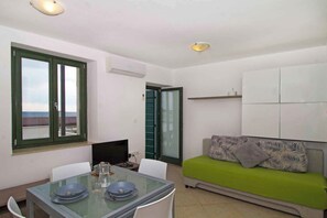 Une pièce comprenant une table à manger, des chaises, un canapé recouvert d’un tissu vert, un téléviseur et une fenêtre donnant sur un beau paysage.