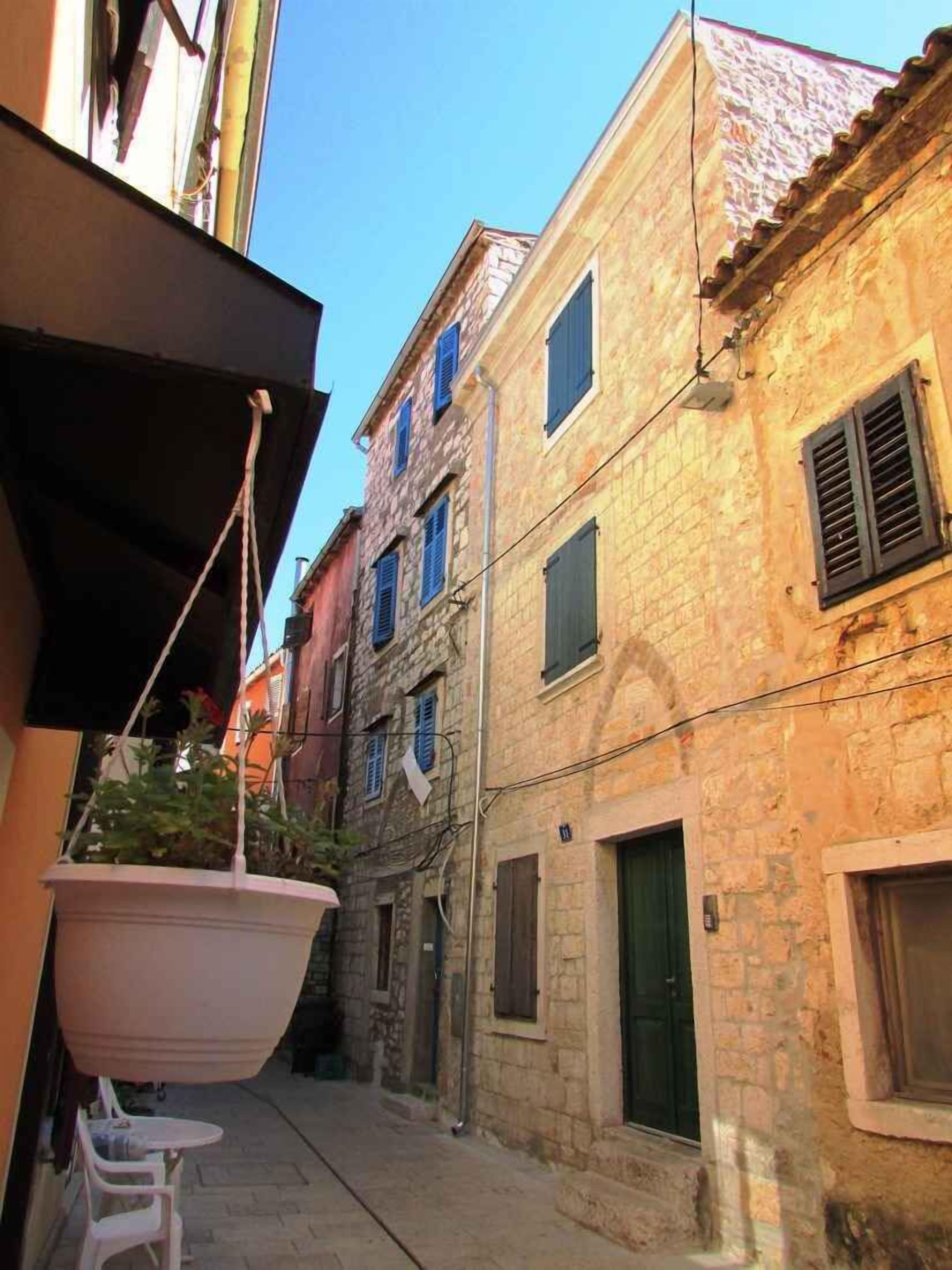Eine enge Gasse mit Steinbauten, einer kleinen Außenbestuhlung und einem Boot im Hintergrund.