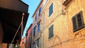 Una calle estrecha con edificios de piedra, un pequeño espacio de asientos al aire libre y un barco visible al fondo.