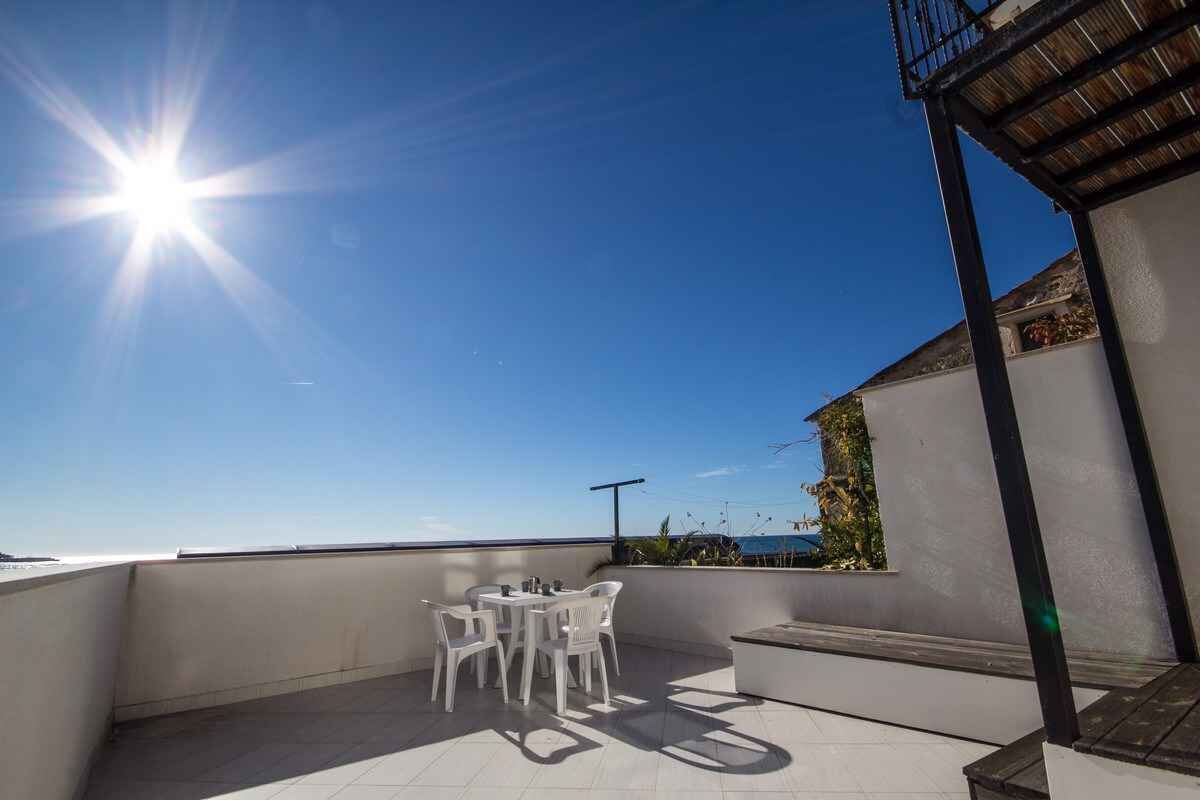 A rooftop terrace with a clear view of the sea, a white table with chairs, and a pergola structure.