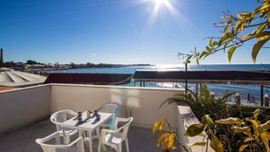 Una terraza con mesa y sillas, con vista a un cuerpo de agua y una costa distante.