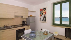 Una cocina con una mesa de comedor, sillas, un refrigerador y una ventana con vista al mar.