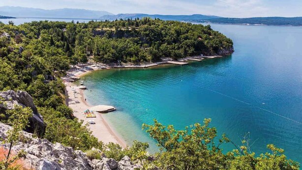 Un paysage côtier comprenant une plage, des eaux cristallines et une zone boisée.