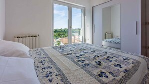 Une chambre avec un grand lit, une armoire, un radiateur et une porte-fenêtre coulissante donnant sur l’extérieur.