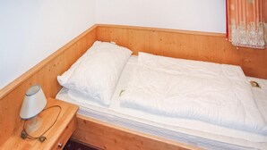 A wooden bunk bed with white bedding, a bedside table with a lamp, and a curtain on the window.