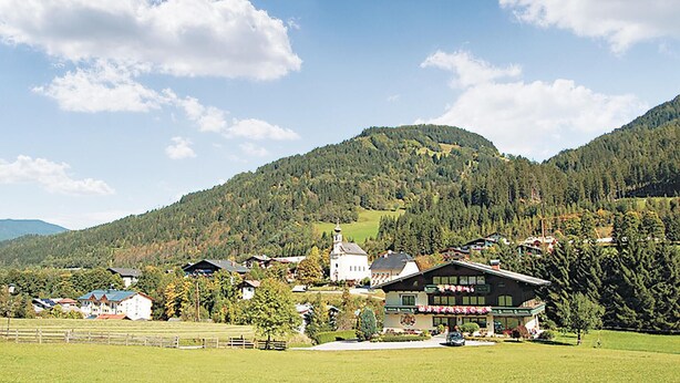 A mountain village with traditional architecture, a church, and a restaurant with outdoor seating.