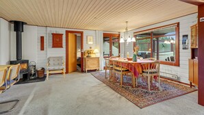 A cozy room with a wooden ceiling, a fireplace, a dining table with chairs, and a large window. - Pet friendly home in Rømø (Rømø)