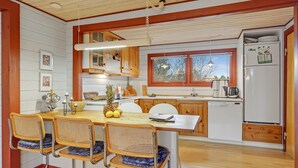 A kitchen with wooden cabinets, a dining table with chairs, a refrigerator, and a window with a view of trees. - Pet friendly home in Rømø (Rømø)