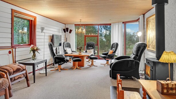 A cozy living room with a fireplace, leather chairs, a wooden table, and large windows offering a view of the outdoors. - Pet friendly home in Rømø (Rømø)