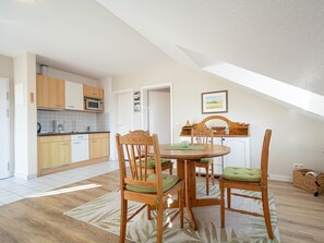 Un coin repas avec une table et des chaises en bois, une cuisine à l’arrière-plan et un plafond en pente.