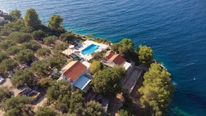 Vue aérienne d’une propriété située sur la côte, avec une piscine, un patio couvert et une maison dont le toit est recouvert de tuiles.