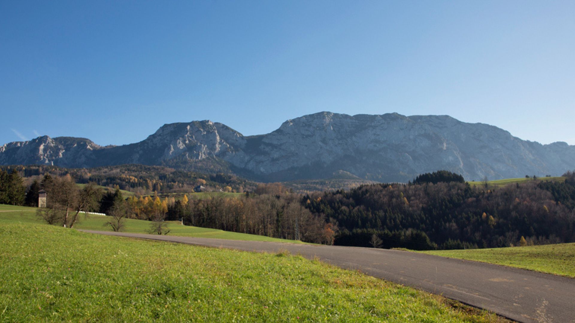 A rural landscape with a road, grassy fields, and mountains in the background.