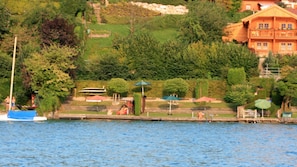 Vista de un lago con una casa de madera, muelle y barcos.