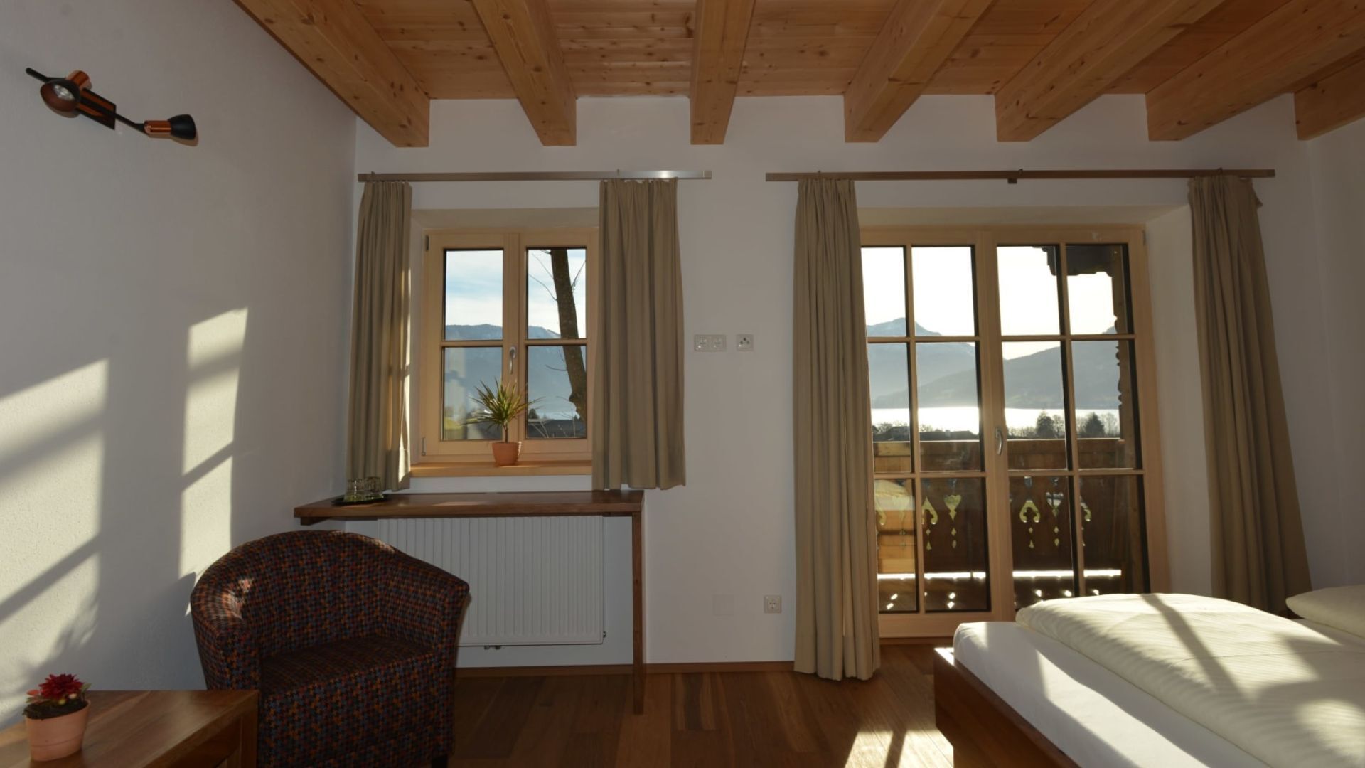 Une chambre à coucher avec un lit, une chaise, une fenêtre avec des rideaux, un radiateur et une vue sur les montagnes.