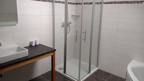 Um banheiro com chuveiro box de vidro, pia e vaso sanitário.