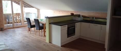 A kitchen with a stove, sink, and cabinets, a dining table with chairs, and a sliding glass door leading outside.