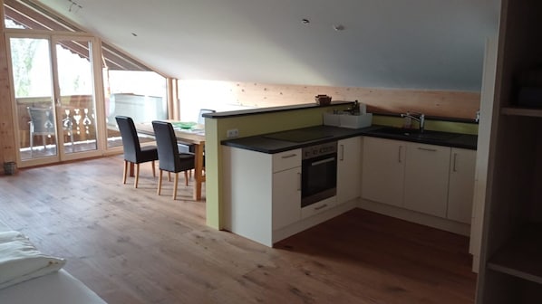 Una cocina con estufa, pileta y alacenas, una mesa de comedor con sillas y un ventanal corredero que da al exterior.