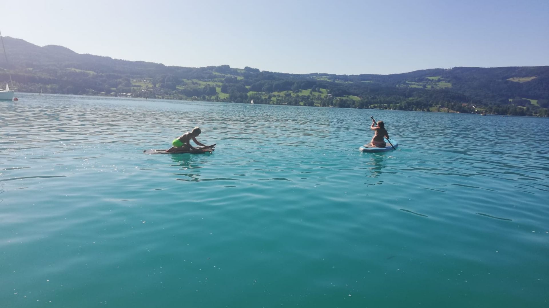 Deux personnes pratiquent le paddle sur un lac paisible, avec un paysage vallonné en arrière-plan.