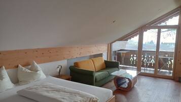 Un dormitorio con una cama, un sofá verde, un cabecero de madera y un ventanal grande.