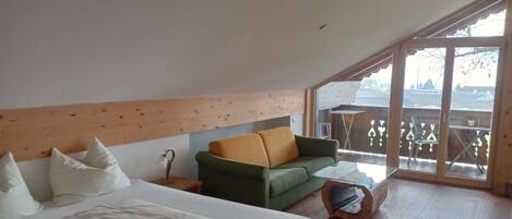 A bedroom with a bed, a green sofa, a wooden headboard, and a large window.