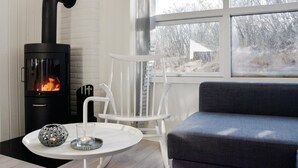 A cozy room with a black wood-burning stove, a white chair, a blue sofa, and a small table with a candle and a decorative item.