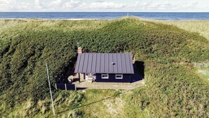 A house with a dark roof, surrounded by grassy terrain and a view of the sea.