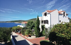 Situated on a hillside overlooking the sea, this coastal property features a two-story building with a red-tiled roof.