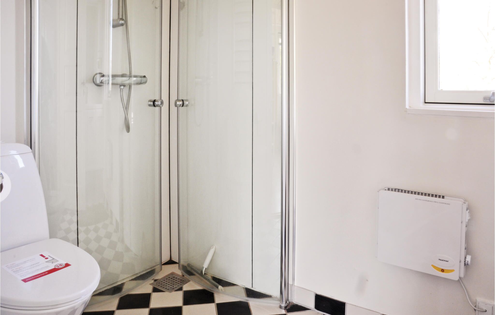 Ein Badezimmer mit Duschkabine aus Glas, einer weißen Toilette und einem Heizkörper an der Wand.