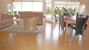 A spacious living room with a wooden floor, a beige sofa, a woven chair, and a dining area with a table and chairs. - 4 bedroom gorgeous home in Bogø By (Bogø By)