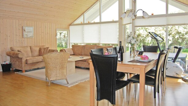 A spacious living area with a wooden ceiling, a sofa, a wicker chair, and a dining table with chairs. - 4 bedroom gorgeous home in Bogø By (Bogø By)