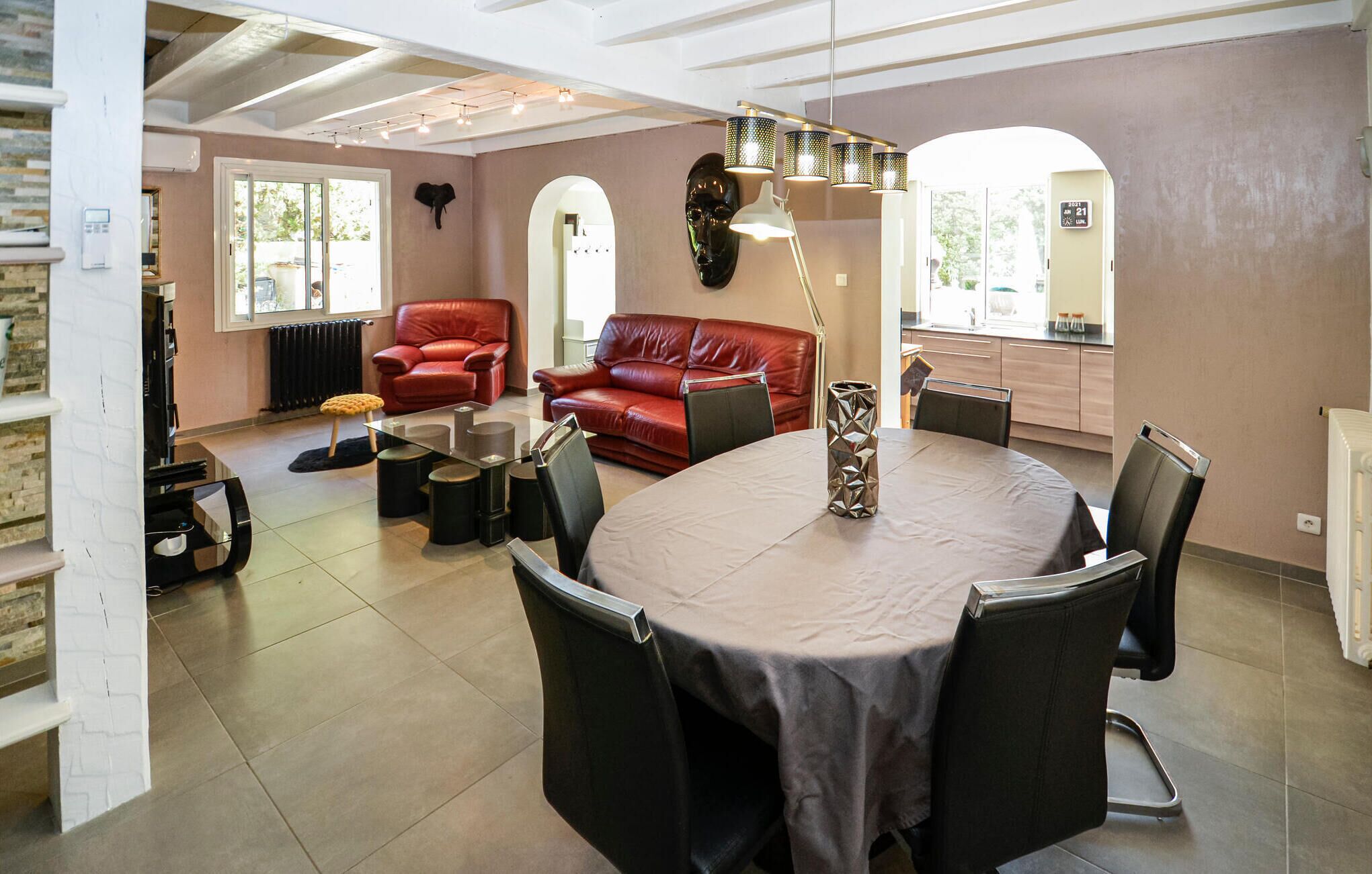 A modern living room with a red leather sofa, a glass coffee table, and a dining table with chairs. There are two elephant head decorations on the walls, and a pendant light hangs above the dining table.