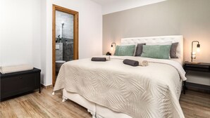 Un dormitorio con una cama grande, una mesita de noche, una puerta de madera y vistas al baño.