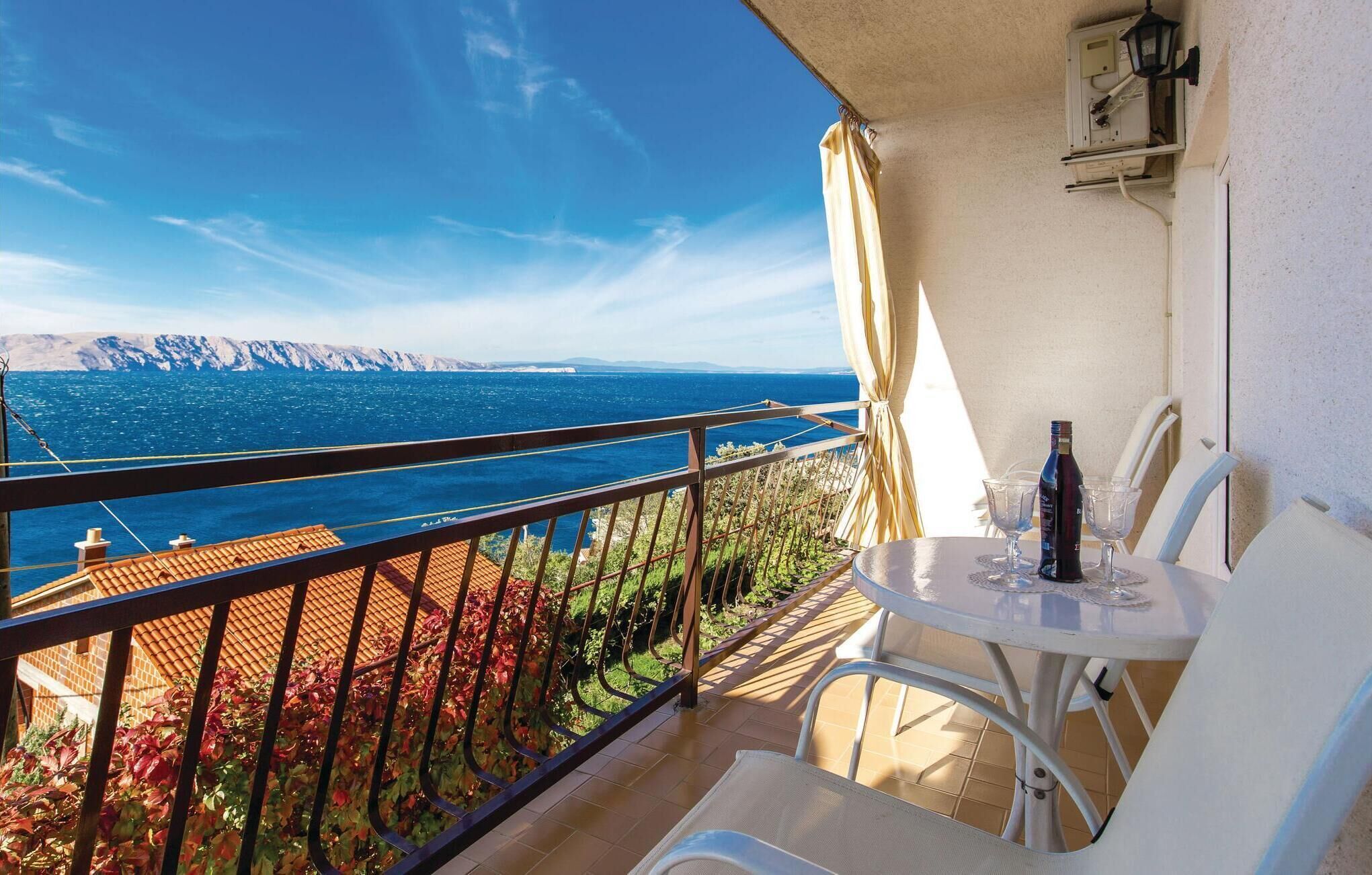 A balcony with a table and chairs, overlooking a scenic view of the sea and mountains.