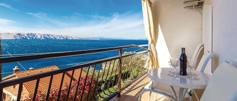 A balcony with a table and chairs, overlooking a scenic view of the sea and mountains.