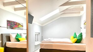 Ett modernt sovrum med ett tak i loftstil, en säng med gröna och gula kuddar och ett litet sängbord.