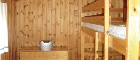 A wooden cabin room with bunk beds, a dresser, and a heater.